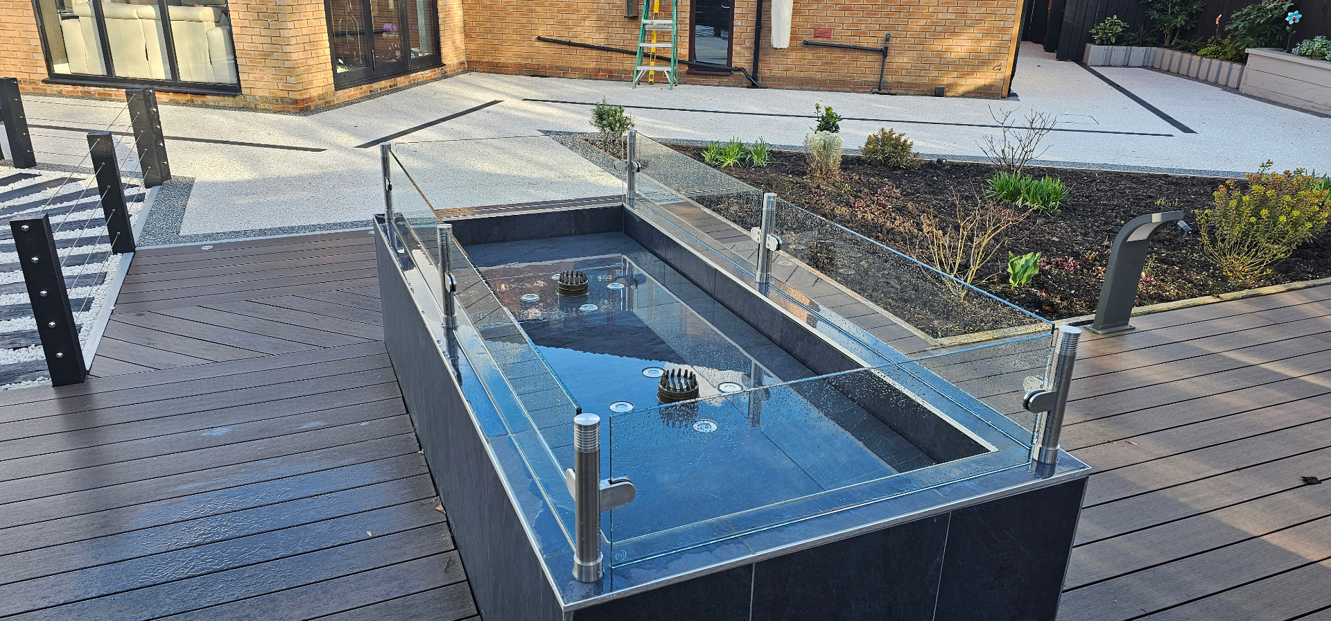 Glass splash guard fitted around a garden water fountain to protect decking from water splashing over the sides